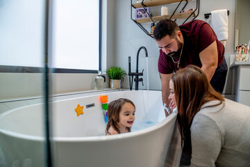 Man and woman bathing toddler girl in bathtub