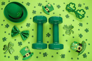 Wall Mural - Two heavy dumbbells, Irish hats with leaf clover, shamrock shaped glasses and a bow tie. Healthy fitness gym flat lay composition concept for St. Patrick's Day.