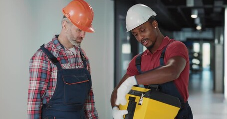 Wall Mural - Couple of heavy indiustry workers preparing for operative work. African man giving instrument tool to his colleague starting work on electric system.