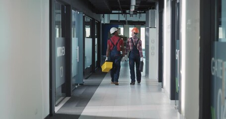 Wall Mural - Couple of professional engineer and his assistant electrician carrying instruments and walking through modern office corridor. Repairing team.