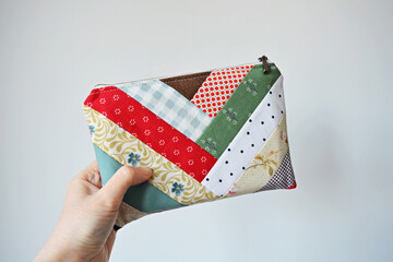 Wall Mural - Hand holding colorful patchwork zipper pouch over white	