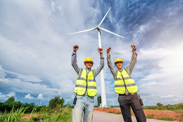 two asian male engineers celebrating success with wind turbine propeller and clear blue sky on the background. Alternative energy, environmental friendly for the future. clean energy innovation.