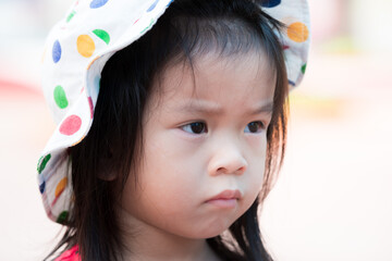 Expression upset child face. Closeup little girl wearing polka dot white hat. Cute kid aged 3-4 years old.