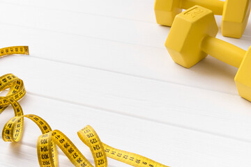 Tape measure and yellow sport equipments on white wooden background