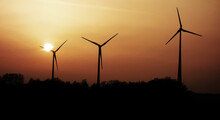 The Silhouettes Of Three Wind Turbines At Sunset.