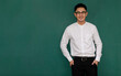 © Bangkok Click Studio - Portrait of young and handsome Asian man wearing eyeglasses and casual business clothes, white shirt and black trousers, standing pose with self-confidence with green background and copy space