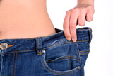 Fototapeta  - Diet concept and weight loss. Young slim woman, in oversize jeans, measuring her waist  on white background