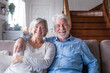 © Daniel - Portrait of happy middle aged retired family couple relaxing on cozy sofa at home. Smiling sincere loving mature senior homeowners looking at camera, posing for photo, showing love and care indoors..