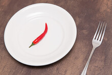 Single One Red Chili Pepper On Empty White Plate And Fork On Table. Spicy Food Concept