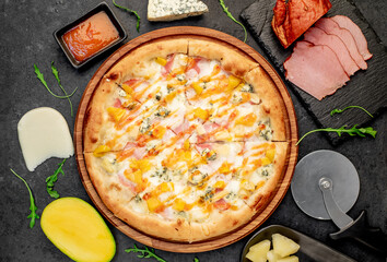 Wall Mural - delicious pizza with ham, cheese, pineapple, mango on a stone background