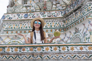 Young Asian women tourist holding coconut and traveling at Wat Arun Ratchawararam, one of the famous places in Bangkok, Thailand