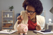© Studio Romantic - Wealth and financial income concept. Closeup portrait of african american woman with wow facial emotion saving money for future putting coin into piggy bank after calculating profit revenue