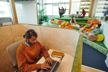 Poster - Young serious mixed-race businessman networking by desk in office environment