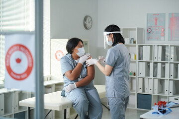 Sticker - Young nurse in uniform and protective workwear making injection to her colleague