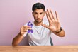 © Krakenimages.com - Young handsome man holding purple ribbon awareness with open hand doing stop sign with serious and confident expression, defense gesture