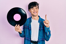 Handsome Hipster Young Man Holding Vinyl Disc Smiling With An Idea Or Question Pointing Finger With Happy Face, Number One
