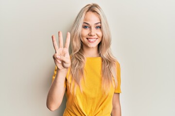 Beautiful caucasian blonde girl wearing casual tshirt showing and pointing up with fingers number three while smiling confident and happy.