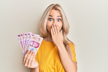 Canvas Print - Beautiful caucasian blonde girl holding 50 mexican pesos banknotes covering mouth with hand, shocked and afraid for mistake. surprised expression