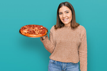 Poster - Young beautiful woman holding italian pizza looking positive and happy standing and smiling with a confident smile showing teeth