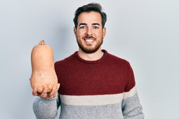 Handsome caucasian man with beard holding healthy fresh pumpkin looking positive and happy standing and smiling with a confident smile showing teeth