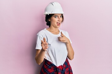 Poster - Young caucasian woman wearing hardhat pointing fingers to camera with happy and funny face. good energy and vibes.