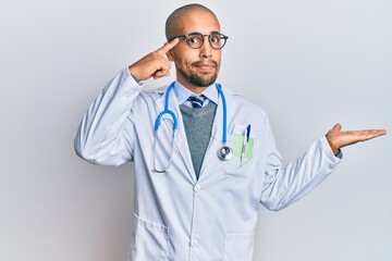 Wall Mural - Hispanic adult man wearing doctor uniform and stethoscope confused and annoyed with open palm showing copy space and pointing finger to forehead. think about it.