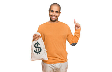 Poster - Hispanic adult man holding dollars bag surprised with an idea or question pointing finger with happy face, number one