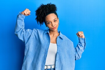 Poster - Young african american girl wearing casual clothes showing arms muscles smiling proud. fitness concept.