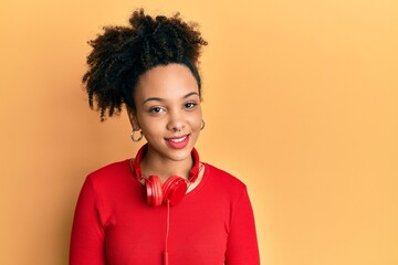 Poster - Young african american girl listening to music using headphones looking positive and happy standing and smiling with a confident smile showing teeth