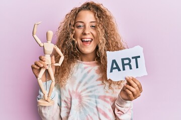 Poster - Beautiful caucasian teenager girl holding wooden manikin and art word smiling and laughing hard out loud because funny crazy joke.