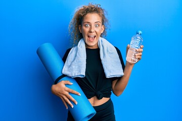 Poster - Beautiful caucasian teenager girl holding yoga mat and water bottle celebrating crazy and amazed for success with open eyes screaming excited.