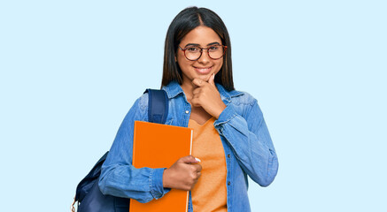 Sticker - Young latin girl wearing student backpack and holding books looking confident at the camera smiling with crossed arms and hand raised on chin. thinking positive.