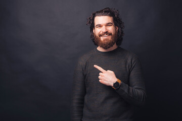 Smiling handsome young bearded man pointing at the corner on copyspace