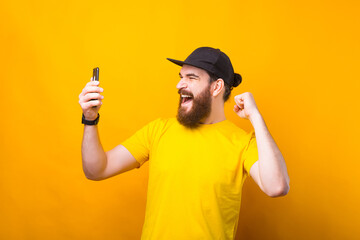 Amazed young man with beard celebrating victory and looking at smartphone