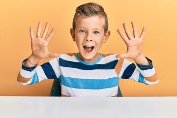 Adorable caucasian kid wearing casual clothes sitting on the table showing and pointing up with fingers number ten while smiling confident and happy.