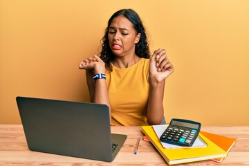 Wall Mural - Young african american girl working at the office with laptop and calculator disgusted expression, displeased and fearful doing disgust face because aversion reaction.