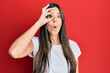 © Krakenimages.com - Young brunette woman wearing casual white tshirt over red background doing ok gesture shocked with surprised face, eye looking through fingers. unbelieving expression.