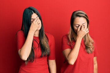 Canvas Print - Hispanic family of mother and daughter wearing casual clothes over red background tired rubbing nose and eyes feeling fatigue and headache. stress and frustration concept.