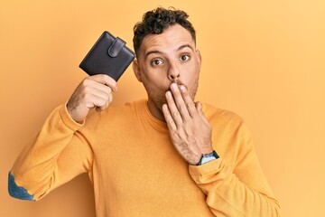 Poster - Young hispanic man holding leather wallet covering mouth with hand, shocked and afraid for mistake. surprised expression