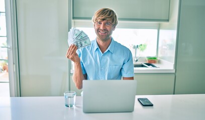 Sticker - Young irish man using laptop holding dollars at home.