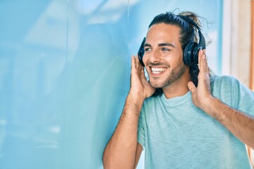 Young hispanic man smiling happy listening to music using headphones at the city.