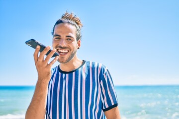 Wall Mural - Young hispanic man smiling happy talking on the smartphone with audio message at the beach.