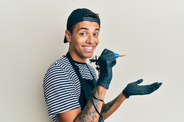 Sticker - Young handsome african american man tattoo artist wearing professional uniform and gloves holding tattooer machine pointing aside with hands open palms showing copy space, presenting advertisement