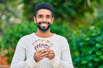 Poster - Young african american man smiling happy holding mexican 500 pesos banknotes at the park.