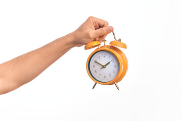 Hand of caucasian young man holding yellow vintage alarm clock over isolated white background