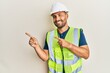© Krakenimages.com - Handsome man with beard wearing safety helmet and reflective jacket smiling and looking at the camera pointing with two hands and fingers to the side.