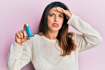 Poster - Beautiful hispanic woman holding medical asthma inhaler stressed and frustrated with hand on head, surprised and angry face