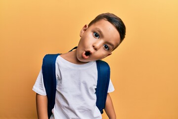 Adorable latin toddler with funny expression wearing student backpack over isolated yellow background.