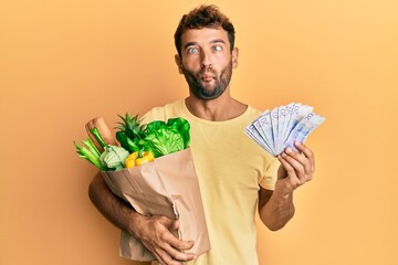 Sticker - Handsome man with beard holding groceries and 20 swedish krona banknotes making fish face with mouth and squinting eyes, crazy and comical.