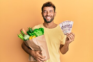 Sticker - Handsome man with beard holding groceries and 500 mexican pesos banknotes smiling with a happy and cool smile on face. showing teeth.